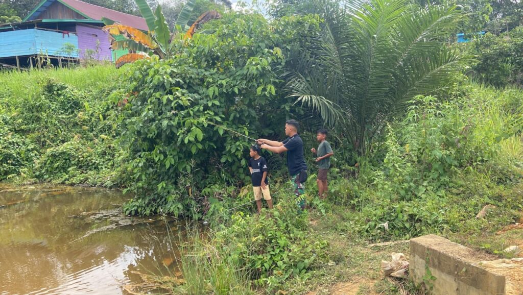 Anggota Satgas TMMD Mengisi Waktu Luang Dengan Memancing Ikan Di Sungai