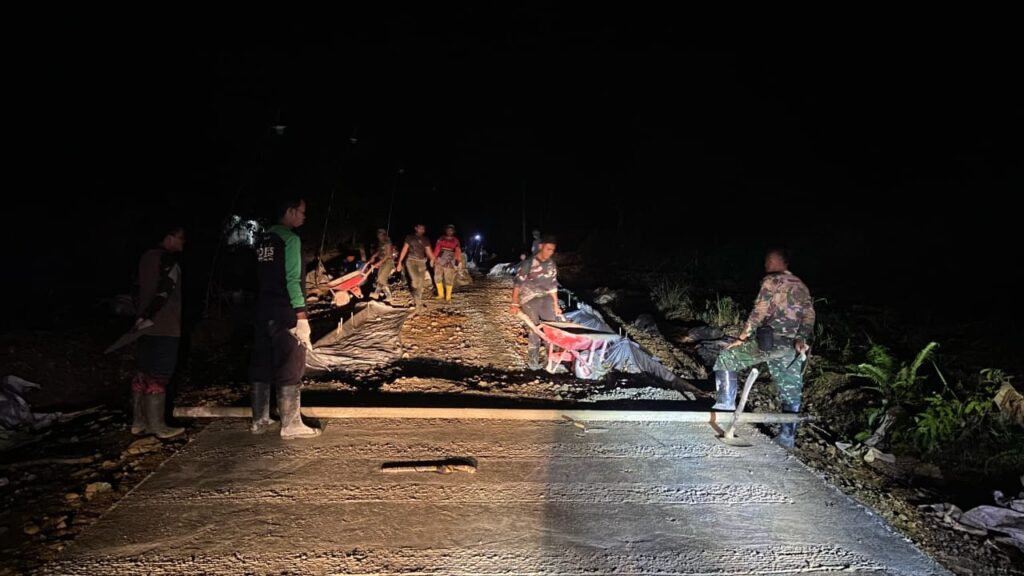 Walaupun Dengan Penerangan Terbatas, Anggota Satgas TMMD Terus Lanjutkan Semenisasi Jalan di Malam Hari